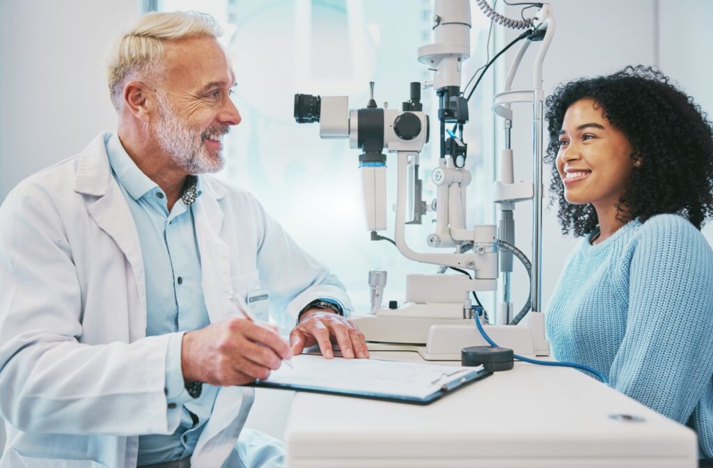 An optometrist and a patient smiling at each other discussing her OHIP coverage during an eye exam.