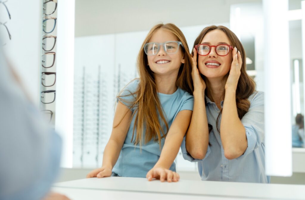 A mother and daughter enjoying a fun moment during their eye exam, trying on glasses together and exploring frame options at the optometry clinic