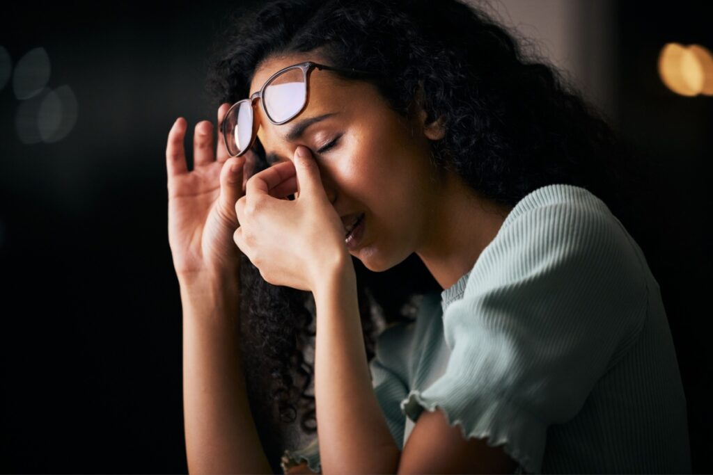 Young woman lifting her glasses and rubbing her eyes due to discomfort or eye strain.