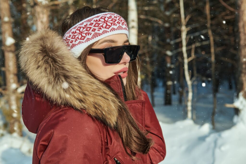 Woman wearing red winter jacket and sunglasses outside during winter.